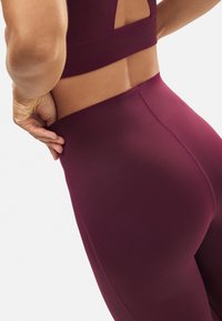 Leggings deportivos burdeos fabricados con tejido suave y elástico. Presentan una cinturilla alta y un diseño sin costuras, que resalta las curvas de las caderas.