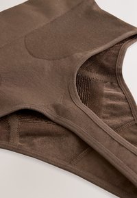 Varrat nélküli barna, magas derekú alakformáló rugalmas bordázott panelekkel a tartásért és a sima felületért, fehér felületen kiterítve.