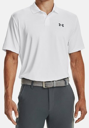 Mężczyzna ubrany w białą koszulkę polo z krótkim rękawem z czarnym logo Under Armour oraz ciemnoszare spodnie z szarym plecionym paskiem.