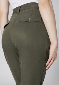 Spodnie w kolorze oliwkowym z wysokim stanem, wykonane z gładkiego materiału, z tylnymi kieszeniami zapinanymi na napy oraz dopasowanym krojem.