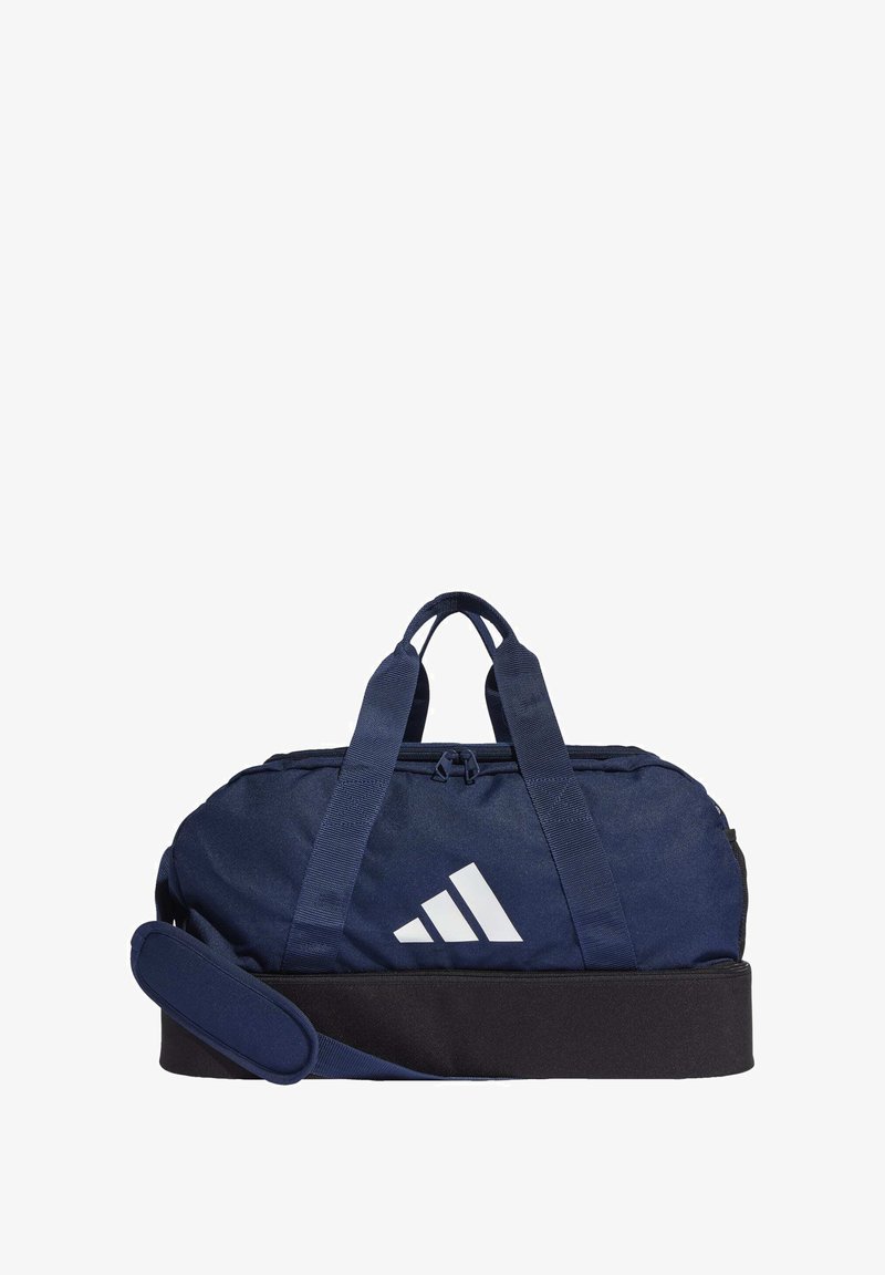 Námorná taška typu duffle s bielym logom, vyrobená z odolného materiálu. Obsahuje dva popruhy, odnímateľný ramenný popruh a zips na zatváranie.