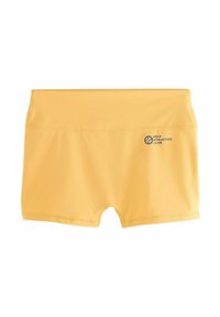 Kollane spordilühike, venivast kangast, keskmise kõrgusega vöökoht ja külgedel sinise värviga trükitud "SELF ATHLETICS CLUB".