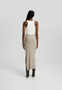 Vit ribbat linne som matchas med en beigefärgad åtsittande maxikjol med en sidoklyfta, bärs tillsammans med bruna knähöga stilettstövlar.