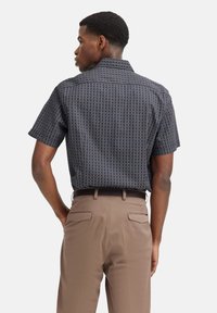 Kurzärmliges Hemd mit Knopfleiste in Dunkelblau mit geometrischem Muster, kombiniert mit braunen Hosen. Mit Kragen und geradem Schnitt.