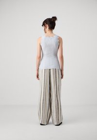 Lyseblå ribbet tanktop med bølgede kanter, kombinert med brede stripete bukser i beige, grå og blå nyanser. Materiale av bomullsblanding.