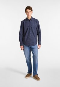 Camicia a maniche lunghe blu navy con un sottile motivo a pois, abbinata a jeans azzurri e scarpe slip-on marroni.