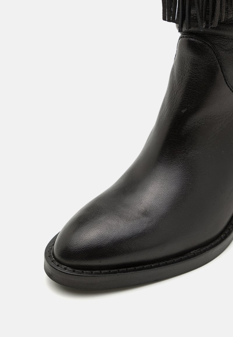 Black leather ankle boot with a pointed toe, textured surface, and contrasting black rubber sole. Features fringe detailing on the shaft.