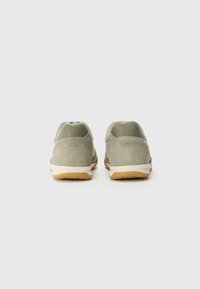 Gray-green suede sneakers with mesh panels, featuring a tan rubber sole and white accents, showing a rounded shape and cushioned heel.