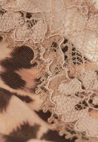 Leopard print fabric with soft texture, featuring delicate beige lace trim with intricate patterns and scalloped edges.