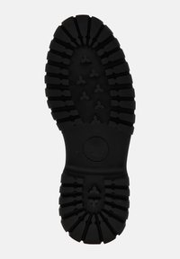 Black rubber shoe sole with deep, textured treads and ridges. Features circular accent and triangular patterns for grip.