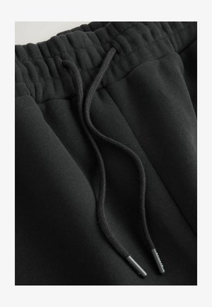 Black jogger pants featuring a textured waistband and external drawstring with black aglets, made from soft, flexible fabric.