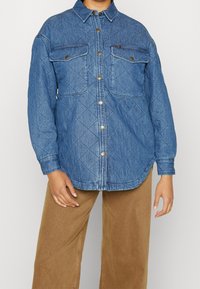 Quiltad denimskjorta i ljusblått, med två framfickor, knappstängning och klassisk krage. Strukturerat tyg med diamantmönster.