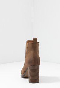 Bottines en faux suède marron avec un bout arrondi, fermeture éclair latérale et un talon chunky strié. Texture lisse avec une silhouette élégante.