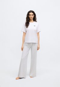 Camiseta blanca de algodón con logo verde en el pecho izquierdo, combinada con pantalones de pierna ancha color gris claro hechos de tela suave.