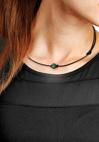 Zwarte koordketting met een centrale groene kraal, ronde vorm, gladde textuur, en vastgezet met twee knopen. Draagt dichtbij de hals.