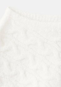 Hvid strikket stof med teksturerede kabelmønstre, blød tekstur og en let dunet finish, foldet ved den ene kant.