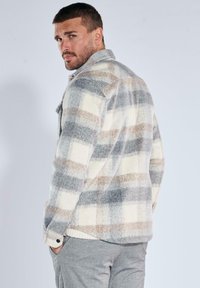 Fleece-Hemdjacke in beige, grau und braun im karierten Muster. Mit einem kragenartigen Ausschnitt, Knopfverschluss und geripptem Saum. Strukturierte Oberfläche.