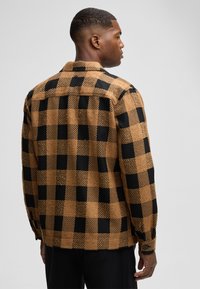 Bruin en zwart geruit shirt gemaakt van een textuurstof. Kenmerkt zich door een kraag en knoopmanchetten, met een ontspannen pasvorm en stevige ontwerp.