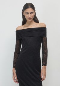 Schwarzes, schulterfreies Kleid mit langen Spitzenärmeln, figurbetonter Silhouette, strukturiertem Blumenmuster und glattem Stoff.