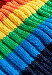 Gebreide stof in levendige regenboogkleuren: rood, oranje, geel, groen, blauw en donkerblauw. Geribbelde textuur met afwisselende strepen.