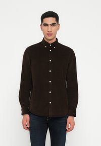 Brun kordfløyelskjorte med knappeskrage, med hvite knapper og lange ermer. Skjorten har rett nederkant og en myk tekstur.