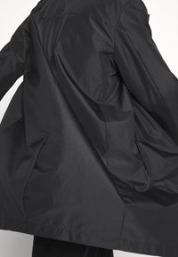 Black, lightweight jacket with a smooth, matte texture. Features a loose fit and wide sleeves, emphasizing a minimalist design.