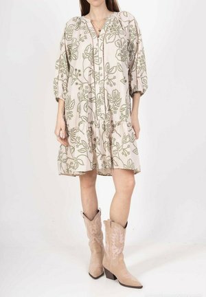 Robe à motifs floraux de couleur rose clair avec un décolleté en V et des manches froncées, dotée d'une jupe à volants. Portée avec des bottes de cowboy beiges.