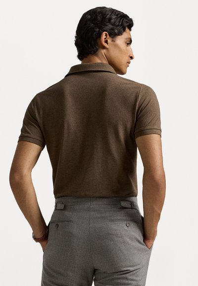 Polo à manches courtes en tissu tricoté marron, avec un col classique. Associé à un pantalon gris, révélant des détails au dos et une coupe ajustée.