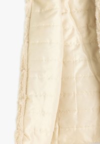 Beige Kunstfell-Außenschicht mit einem glatten, cremigen Innenraum. Der Innenraum verfügt über gesteppten, gepolsterten Abschnitte zur Isolierung.