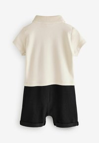 Mono de manga corta en crema y negro. Presenta un cuello tipo polo, diseño a bloques de color y puños enrollados en los pantalones cortos. Material texturizado.