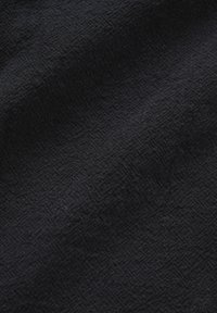 Black textured fabric with a subtle geometric pattern, shown in close-up with soft folds and shadows.