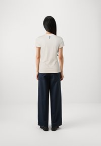 Camiseta beige de manga corta con un diseño de signo de interrogación en la parte posterior. Combina con pantalones de pierna ancha azul oscuro y zapatos negros.