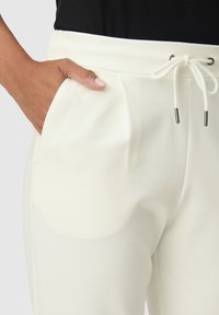 Witte sweatpants met een gladde textuur, met zijzakken en een verstelbare tailleband met metalen accenten. De stof lijkt zacht en licht van gewicht te zijn.