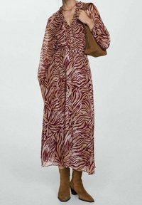 Femme portant une robe à manches longues, boutonnée, à motif zèbre, avec des bottines en daim marron et une sacoche en daim marron.