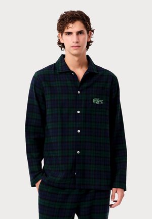 Haut de pyjama en flanelle à carreaux verts et marine avec des manches longues, fermeture à boutons et logo brodé sur la poitrine. Texture douce.