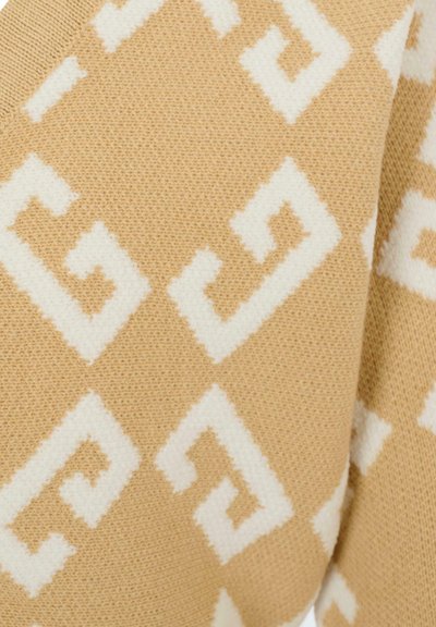Tessuto lavorato a maglia beige con motivi geometrici bianchi a forme angolari e una consistenza morbida. Dettaglio ravvicinato che mette in risalto la profondità del design.