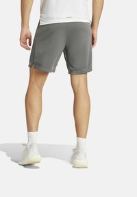 Pantalones cortos atléticos grises hechos de una tela suave, con un ajuste relajado, aberturas laterales y cortos por encima de las rodillas. Calcetines y zapatos blancos visibles.