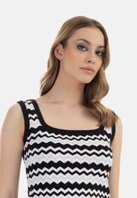 Top fără mâneci cu un model în zigzag alb-negru, având decolteu pătrat. Materialul pare neted și elastic.