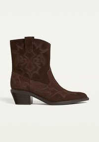 Dark brown suede ankle boot with Western-style stitching, mid-height stacked heel, and pull tab on the shaft.
