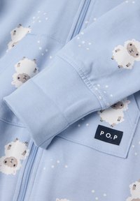 Lichtblauwe fleece zip-up kleding met patronen van cartoon schapen en witte stippen. Label op de zak zegt "P.O.P." met een marineblauwe achtergrond.