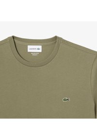 T-shirt verde oliva di taglio regolare, realizzata in 100% cotone Pima. Presenta un collo rotondo e un logo coccodrillo ricamato sul petto.