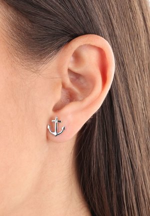 Pendiente de aro de plata exhibido en la oreja de un modelo, mostrando un acabado pulido, diseño esbelto y un pequeño detalle de cruz en la parte superior.
