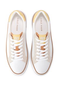 Sneakers bianchi in pelle con dettagli in suede beige, rifiniture gialle e lacci bianchi. Suola in gomma marrone con una finitura testurizzata.