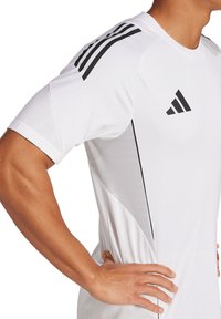T-shirt de sport blanc avec des accents noirs. Présente des panneaux latéraux en maille et trois bandes noires sur l'épaule. Matériel en polyester, design ajusté.
