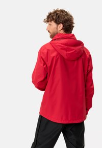 Giacca impermeabile rossa con cappuccio, caratterizzata da una texture liscia e una vestibilità comoda, abbinata a pantaloni neri.
