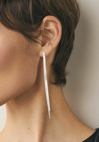 Langsølvøreringe med et slankt, forlænget design, der har en glat tekstur og minimal hardware, der hænger under øret.