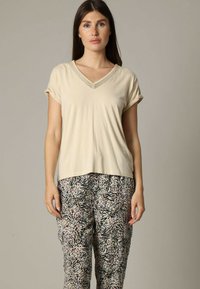 T-shirt beige clair en V avec des manches retroussées, associé à un pantalon ample à motifs présentant des designs abstraits noirs, roses et crème.