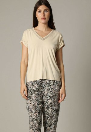 Lichtbeige V-hals t-shirt met opgerolde mouwen, in combinatie met patroonrijke, losse broek met abstracte ontwerpen in zwart, roze en crèmekleur.