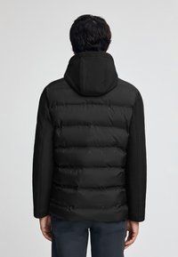 Svart puffjacka med huva, med en vadderad design och slät tyg, strukturerad passform och långa ärmar. Bakvy visas.