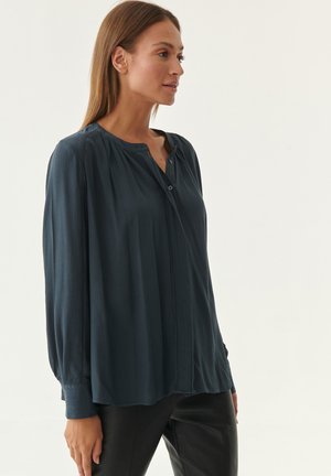 Dark teal button-up blouse with a pleated design, long sleeves, and a rounded neckline featuring decorative button accents. Smooth fabric texture.